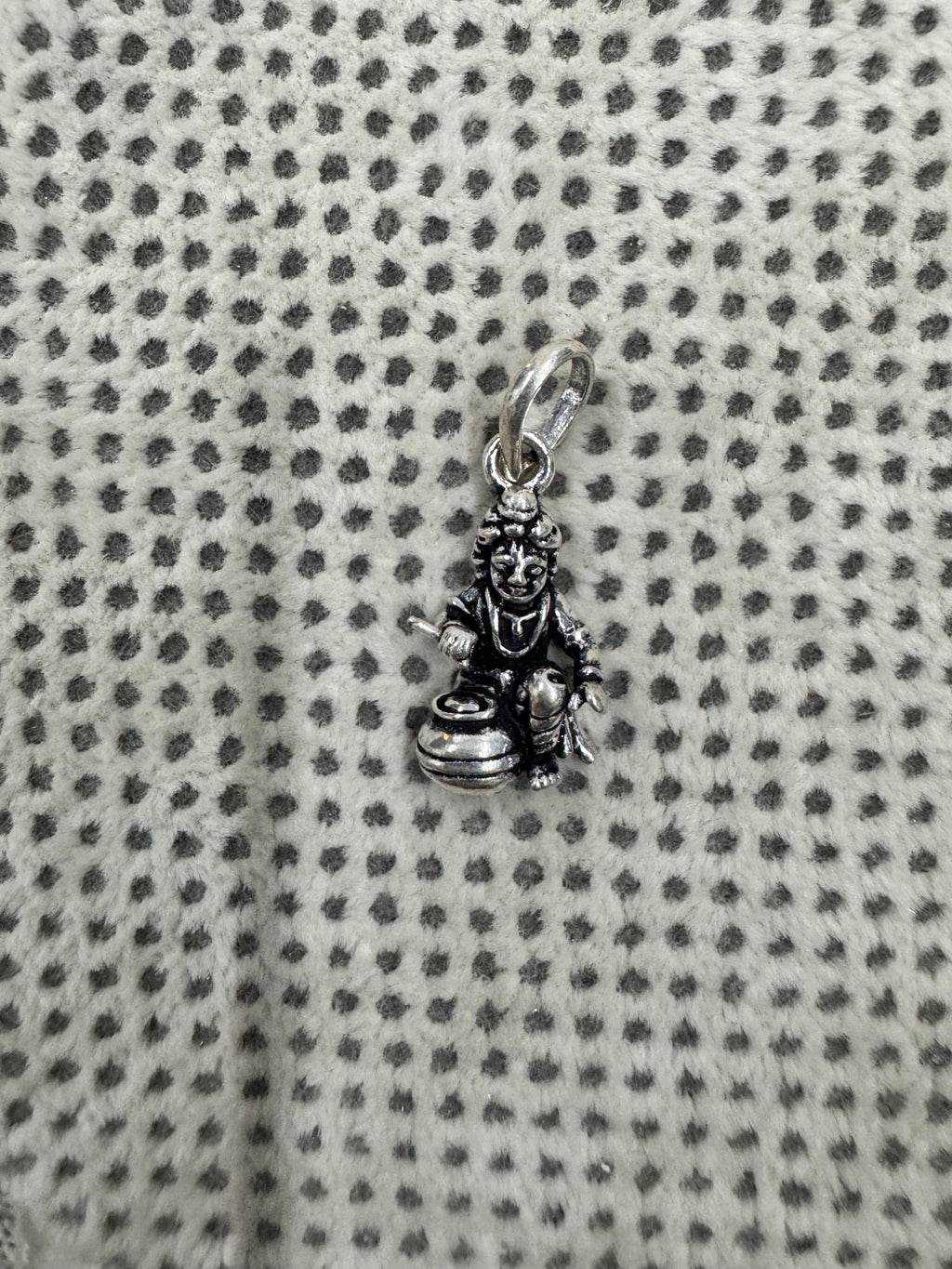 Full length of the sterling silver pendant with its oval bail and jump ring, laid on grey dotted fabric.
