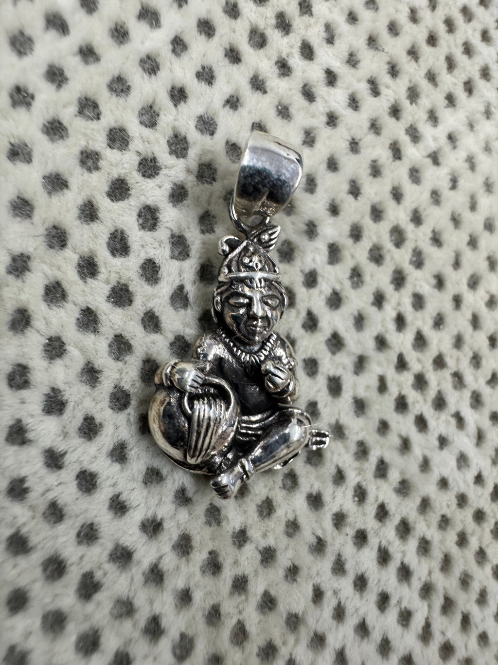 Angled view of the sterling silver pendant, the raised fist and the folded legs seen from the side.