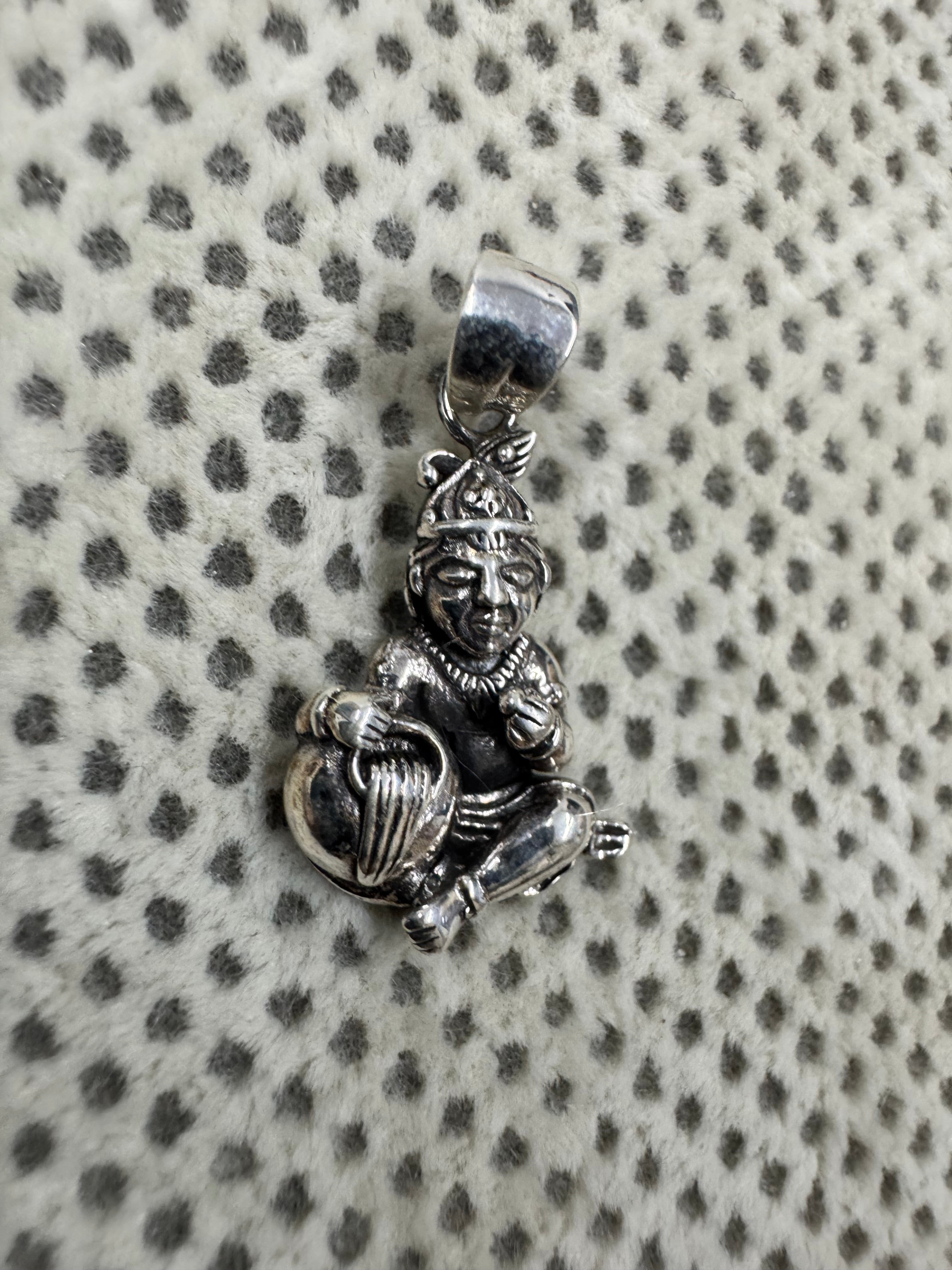 Angled view of the sterling silver pendant, the raised fist and the folded legs seen from the side.