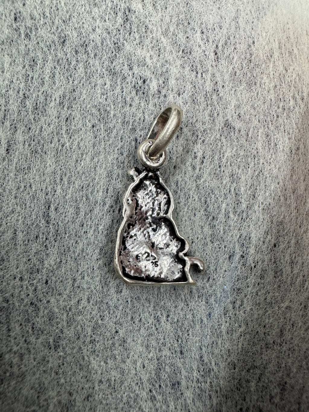 Reverse of the bright sterling silver Ganesha pendant on grey speckled card, showing the hollow casting and the jump ring.
