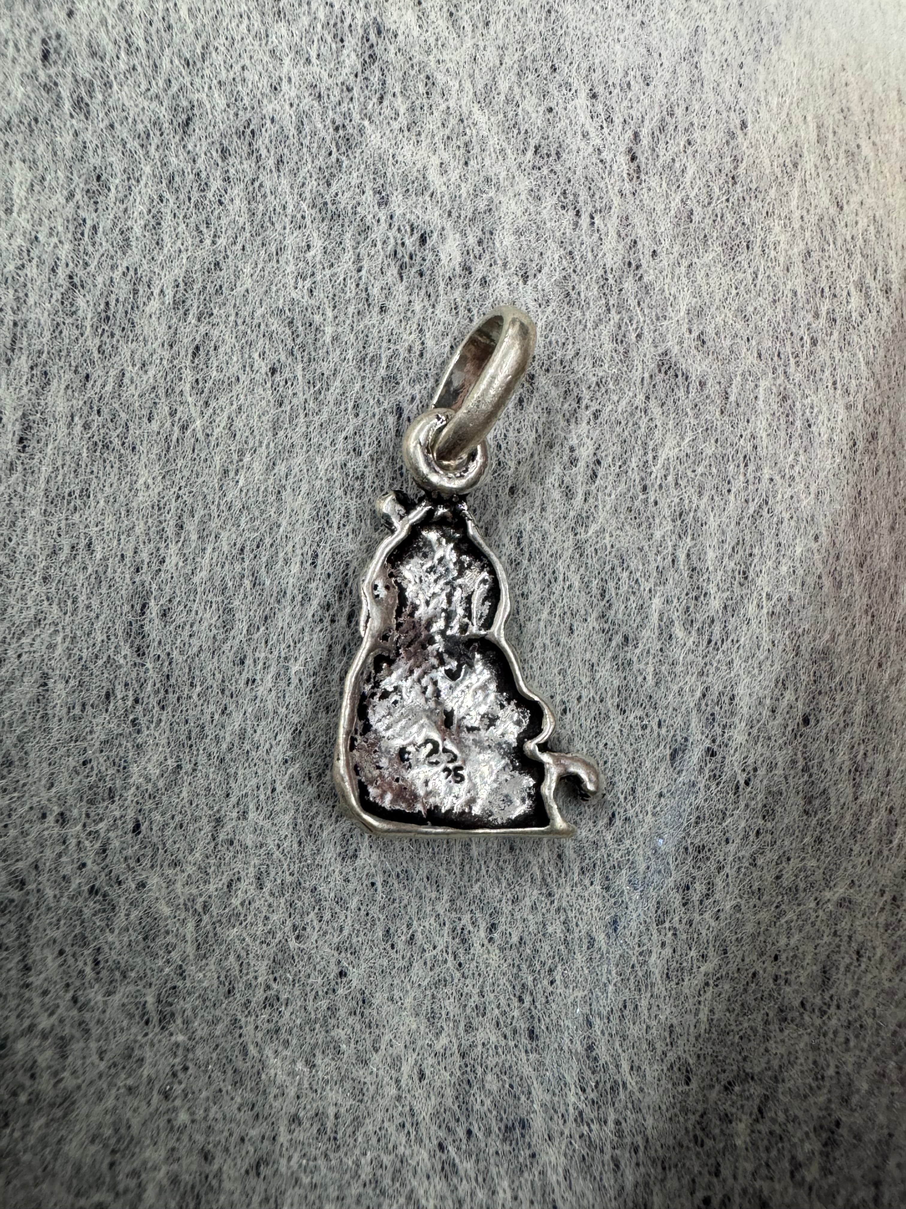 Reverse of the bright sterling silver Ganesha pendant on grey speckled card, showing the hollow casting and the jump ring.