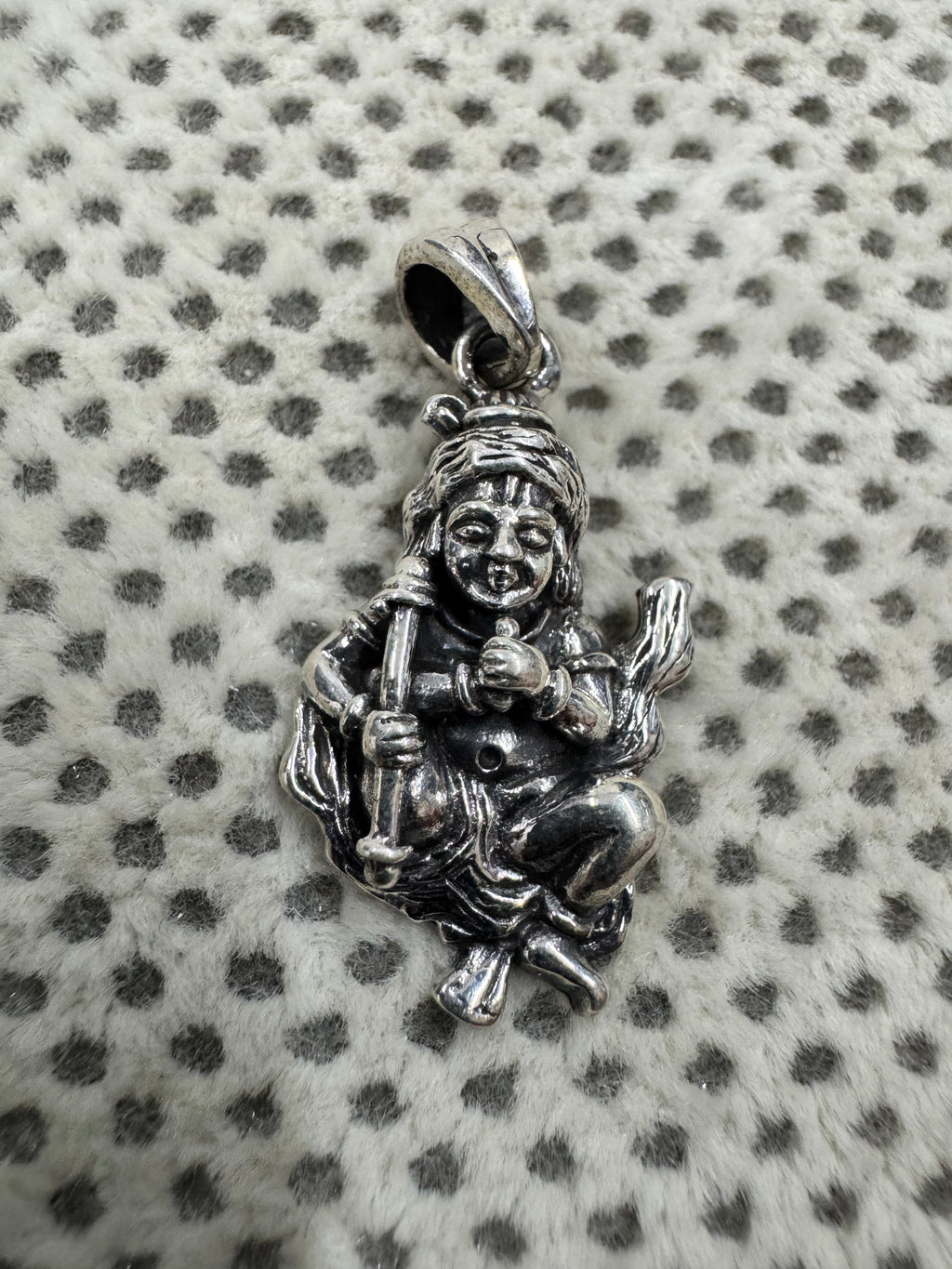 Oxidised sterling silver krishna pendant on grey dotted fabric, showing the topknot, the scored brow.