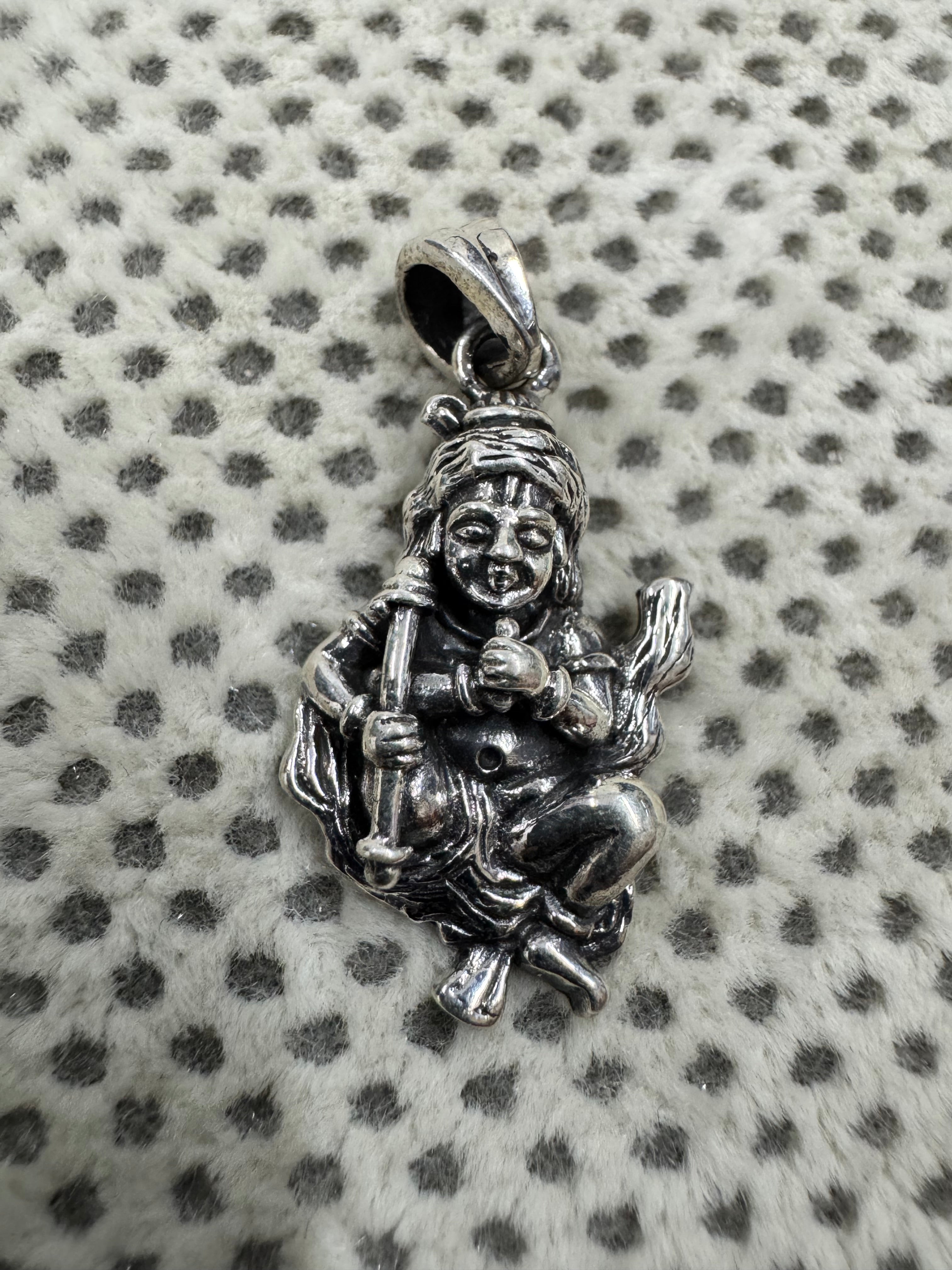 Oxidised sterling silver krishna pendant on grey dotted fabric, showing the topknot, the scored brow.