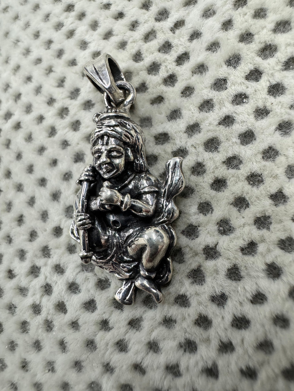 Angled view of the sterling silver gwala krishan pendant on dotted fabric, the flat tapered bail turned to the camera.