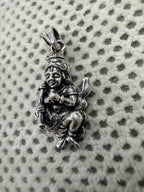 Angled view of the sterling silver gwala krishan pendant on dotted fabric, the flat tapered bail turned to the camera.