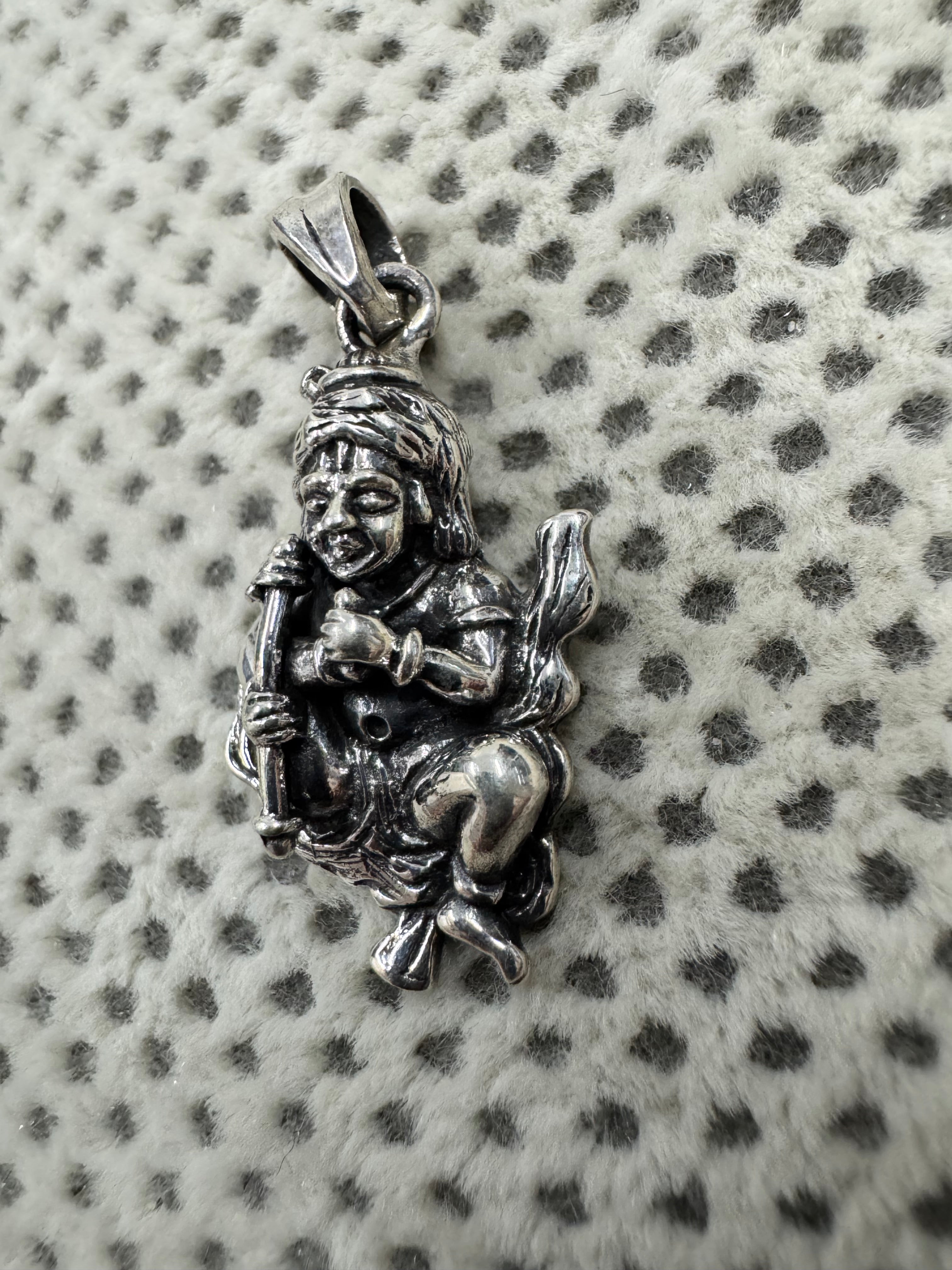 Angled view of the sterling silver gwala krishan pendant on dotted fabric, the flat tapered bail turned to the camera.