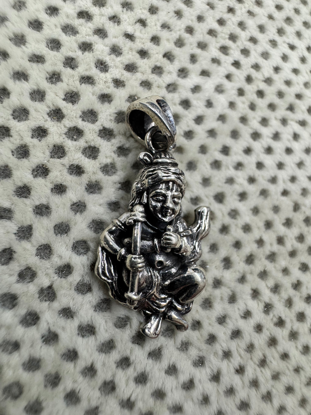 Sterling silver krishna pendant on dotted fabric, the hearding stick lying diagonally across the folded legs.