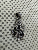 Sterling silver krishna pendant on dotted fabric, the hearding stick lying diagonally across the folded legs.