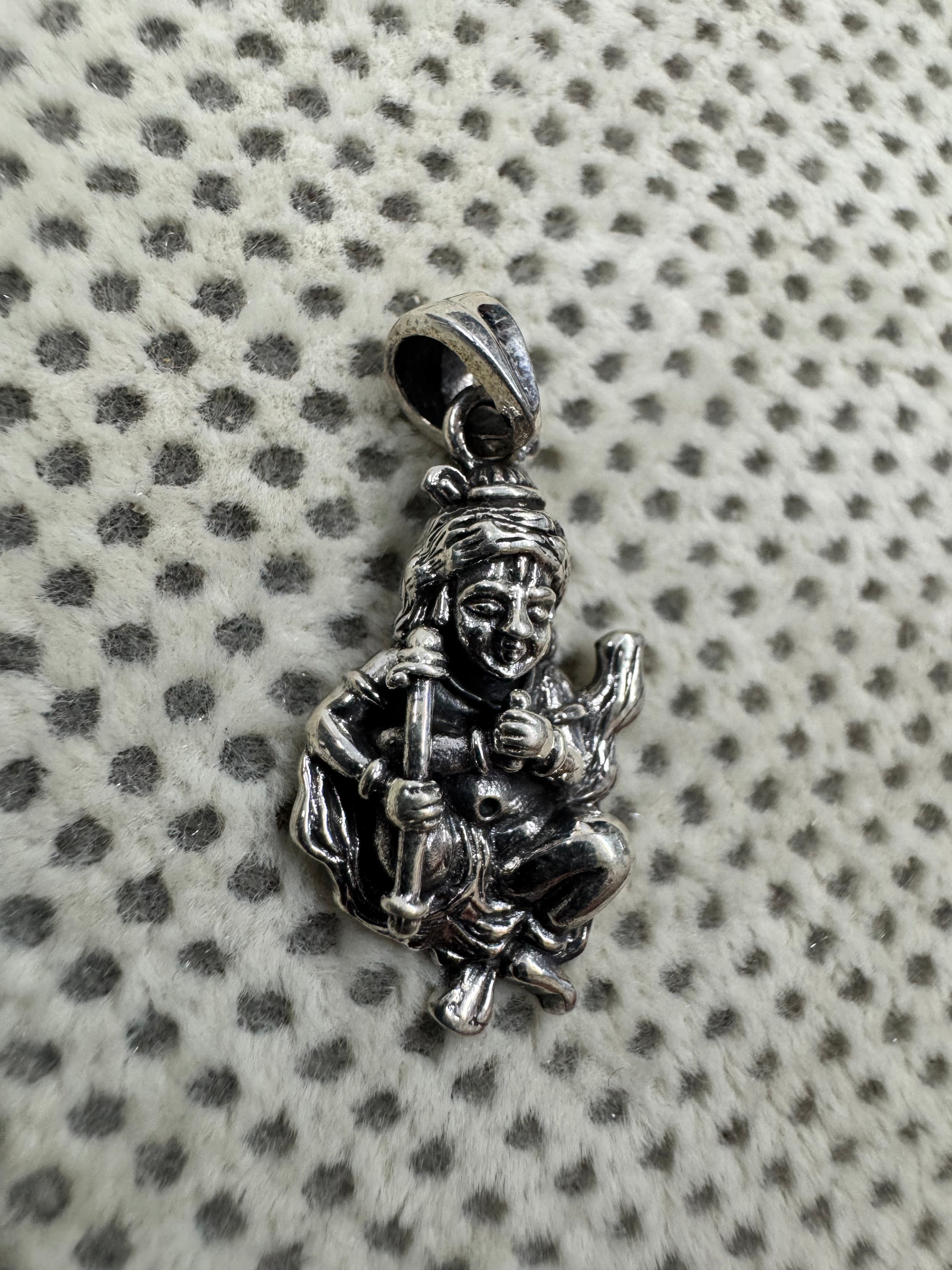 Sterling silver krishna pendant on dotted fabric, the hearding stick lying diagonally across the folded legs.
