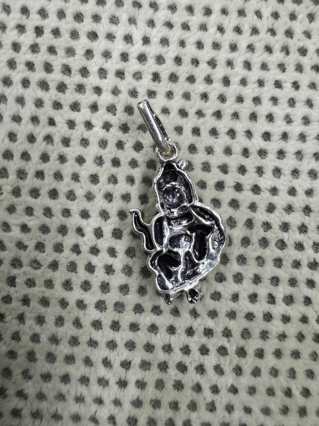 Reverse of the sterling silver gwala krishan pendant on dotted fabric, showing the hollowed back of the casting.