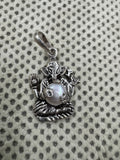 Sterling silver Ganesha pendant with a round pearl set as the belly, laid on grey dotted fabric.