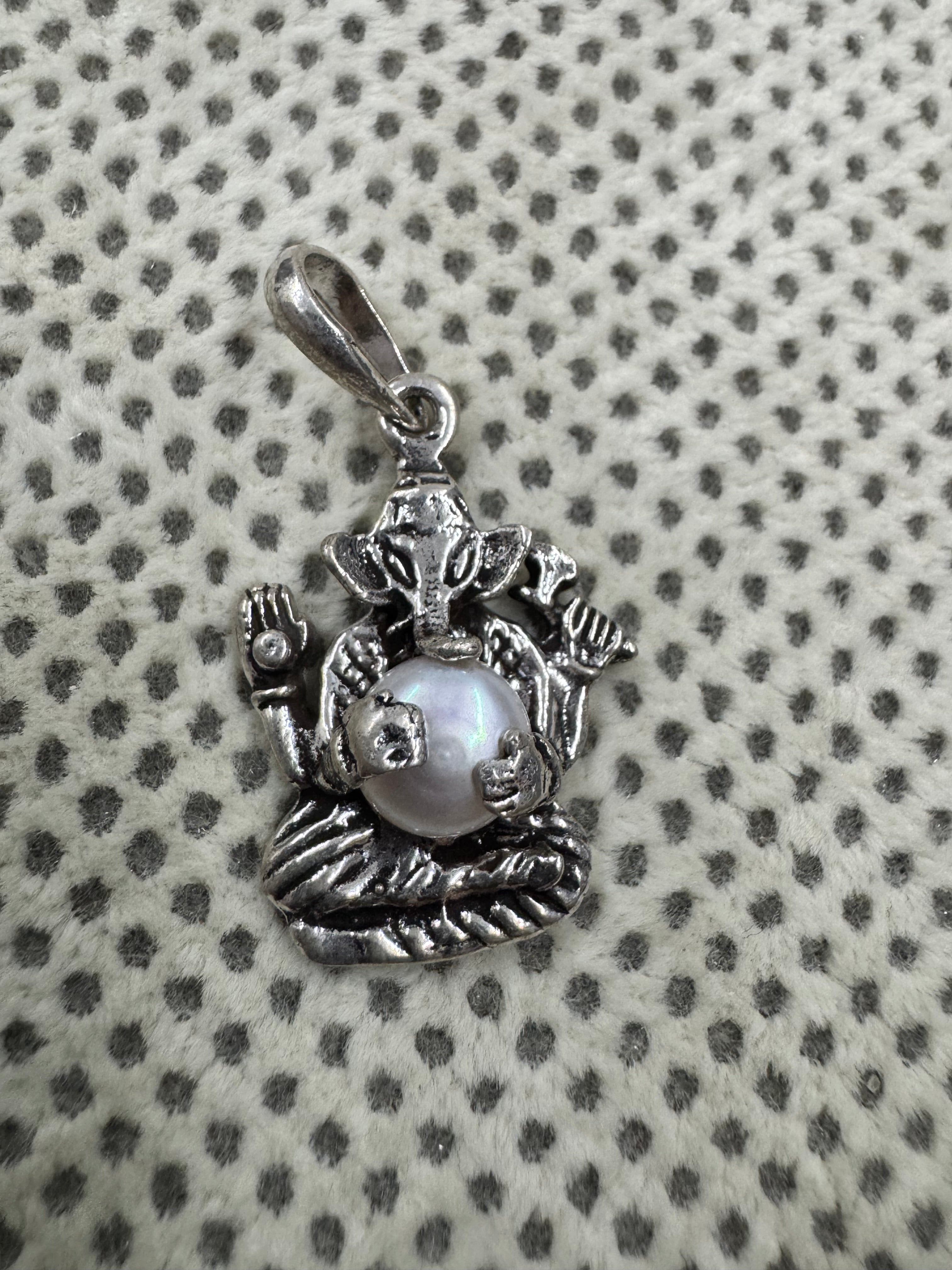 Sterling silver Ganesha pendant with a round pearl set as the belly, laid on grey dotted fabric.