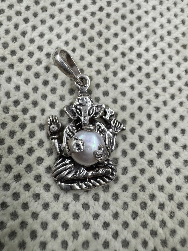 Sterling silver Ganesha pendant with a round pearl set as the belly, laid on grey dotted fabric.