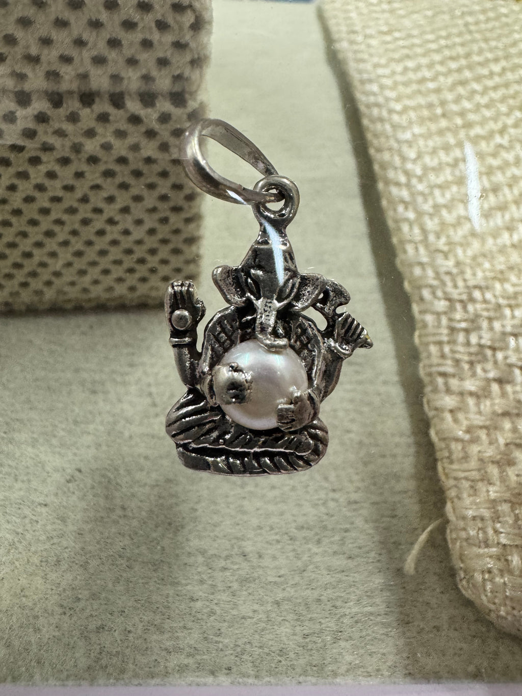 Angled view of the sterling silver Ganesha pendant with pearl, showing the ears, the four arms and the ribbed base.