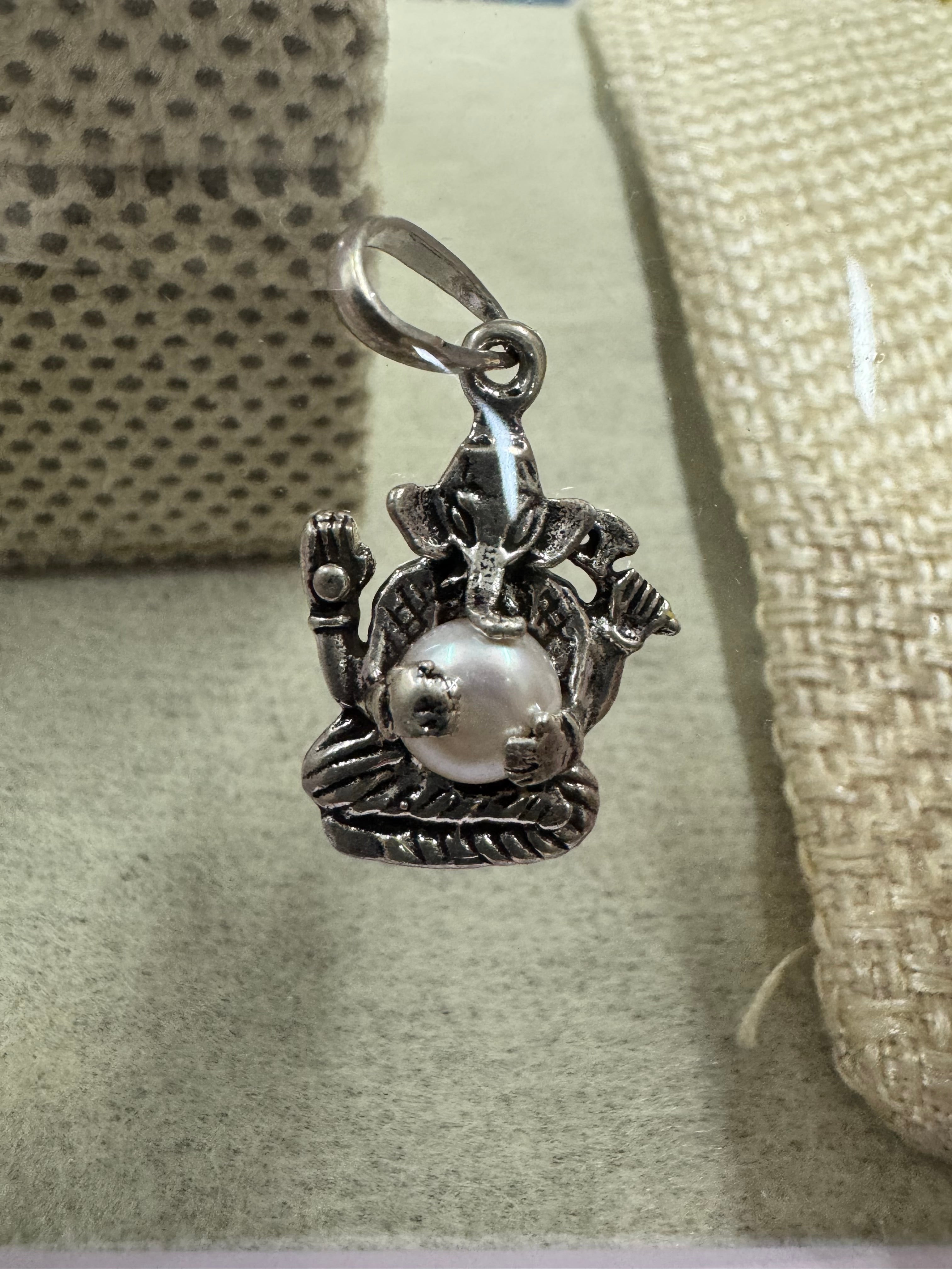 Angled view of the sterling silver Ganesha pendant with pearl, showing the ears, the four arms and the ribbed base.