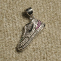Sterling silver high-top trainer Pendant Bejewelled-set with cubic zirconia, with blush-pink and green cubic zirconia accents and a contrast black motif, on a beige woven backdrop.