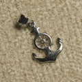 Polished sterling silver Pendant of an anchor crossed with a ship's wheel, resting on a beige woven backdrop.