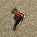 Sterling silver high-top trainer Pendant with glossy red and black panels and a white midsole line, on a beige woven backdrop.