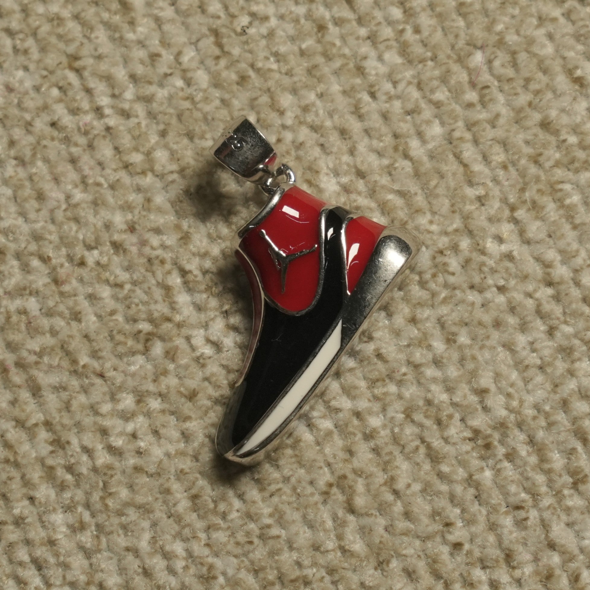 Sterling silver high-top trainer Pendant with glossy red and black panels and a white midsole line, on a beige woven backdrop.