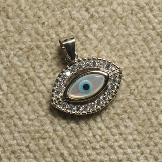 Sterling silver evil eye Pendant with a pale iridescent eye centre and a border of cubic zirconia, photographed on beige woven fabric.