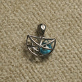 Sterling silver half-moon openwork cage Pendant holding a turquoise-blue eye bead, photographed on beige woven fabric.