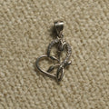 Sterling silver open heart Pendant with a sculpted rose motif and a line of cubic zirconia along one edge, photographed on beige woven fabric.