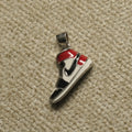 Sterling silver high-top sneaker Pendant with red, black and off-white enamel panels, photographed on beige woven fabric.