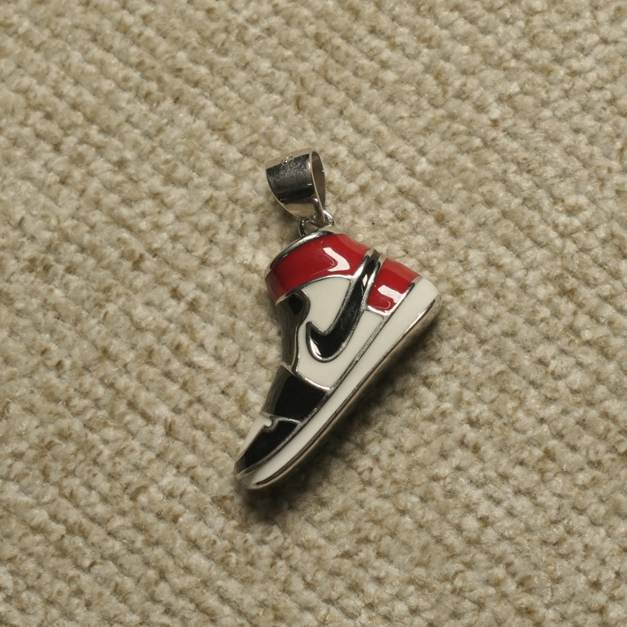 Sterling silver high-top sneaker Pendant with red, black and off-white enamel panels, photographed on beige woven fabric.