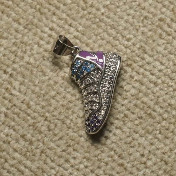 Sterling silver sneaker Pendant covered in clear, blue and violet cubic zirconia with a lilac enamel collar, photographed on beige woven fabric.