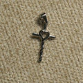 Polished sterling silver cross Pendant with an open heart at the centre and a twisted lower stem, photographed on beige woven fabric.