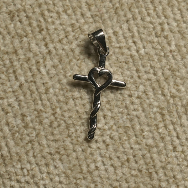 Polished sterling silver cross Pendant with an open heart at the centre and a twisted lower stem, photographed on beige woven fabric.