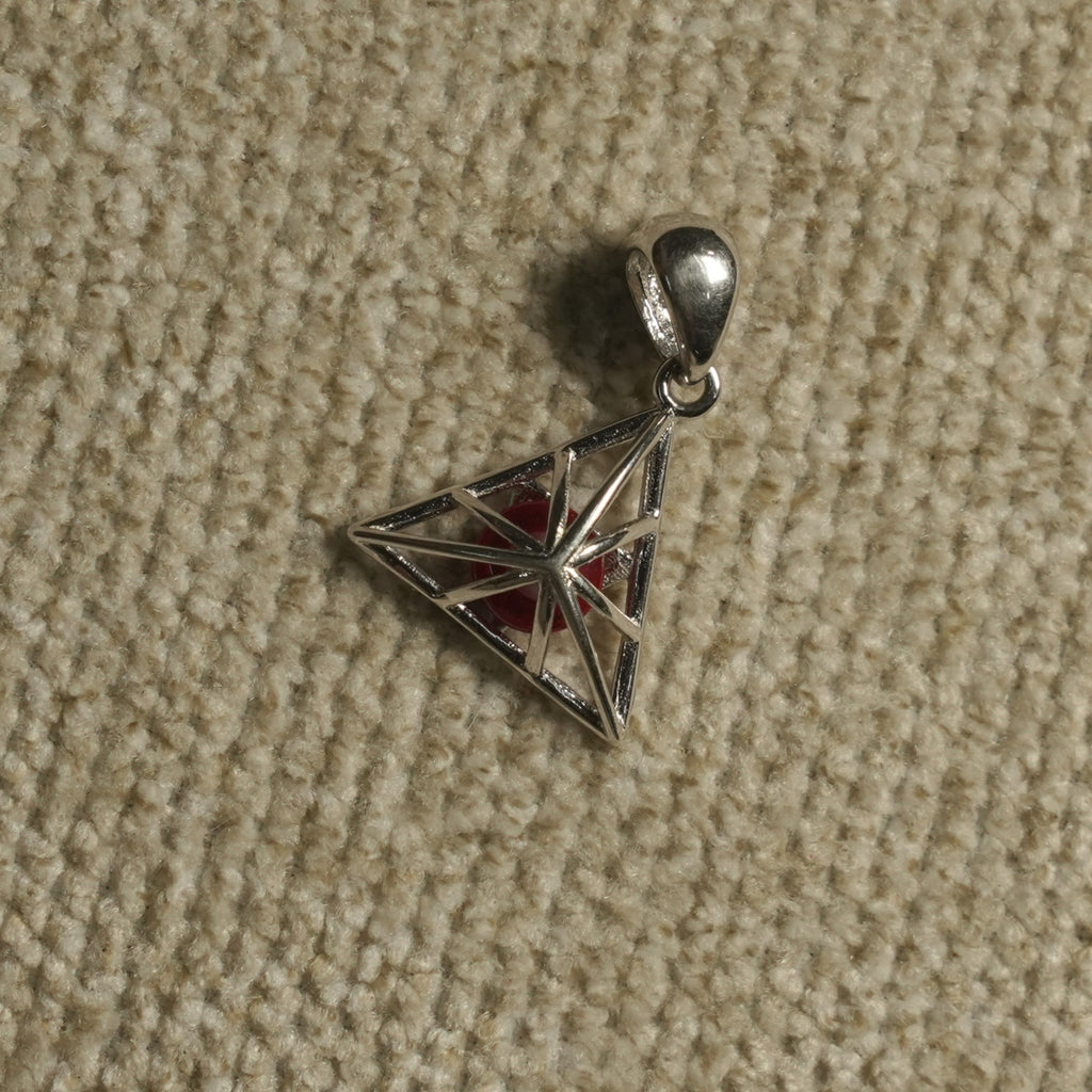 Angled view of the sterling silver triangle cage Pendant showing its star-like lattice, red centre bead and polished bail.