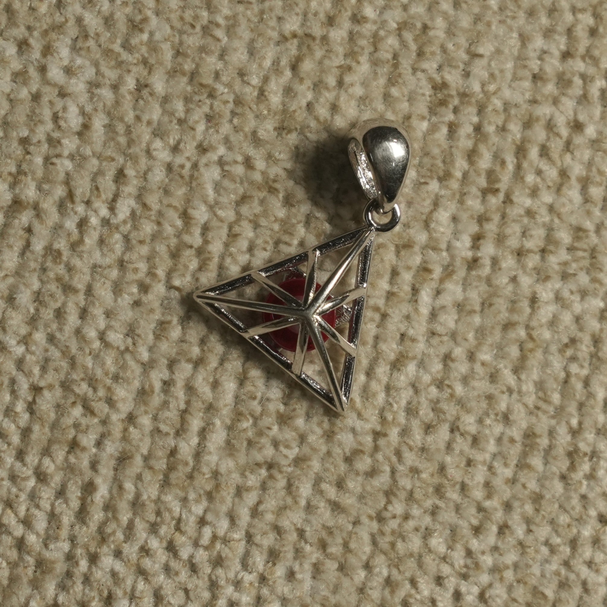 Angled view of the sterling silver triangle cage Pendant showing its star-like lattice, red centre bead and polished bail.