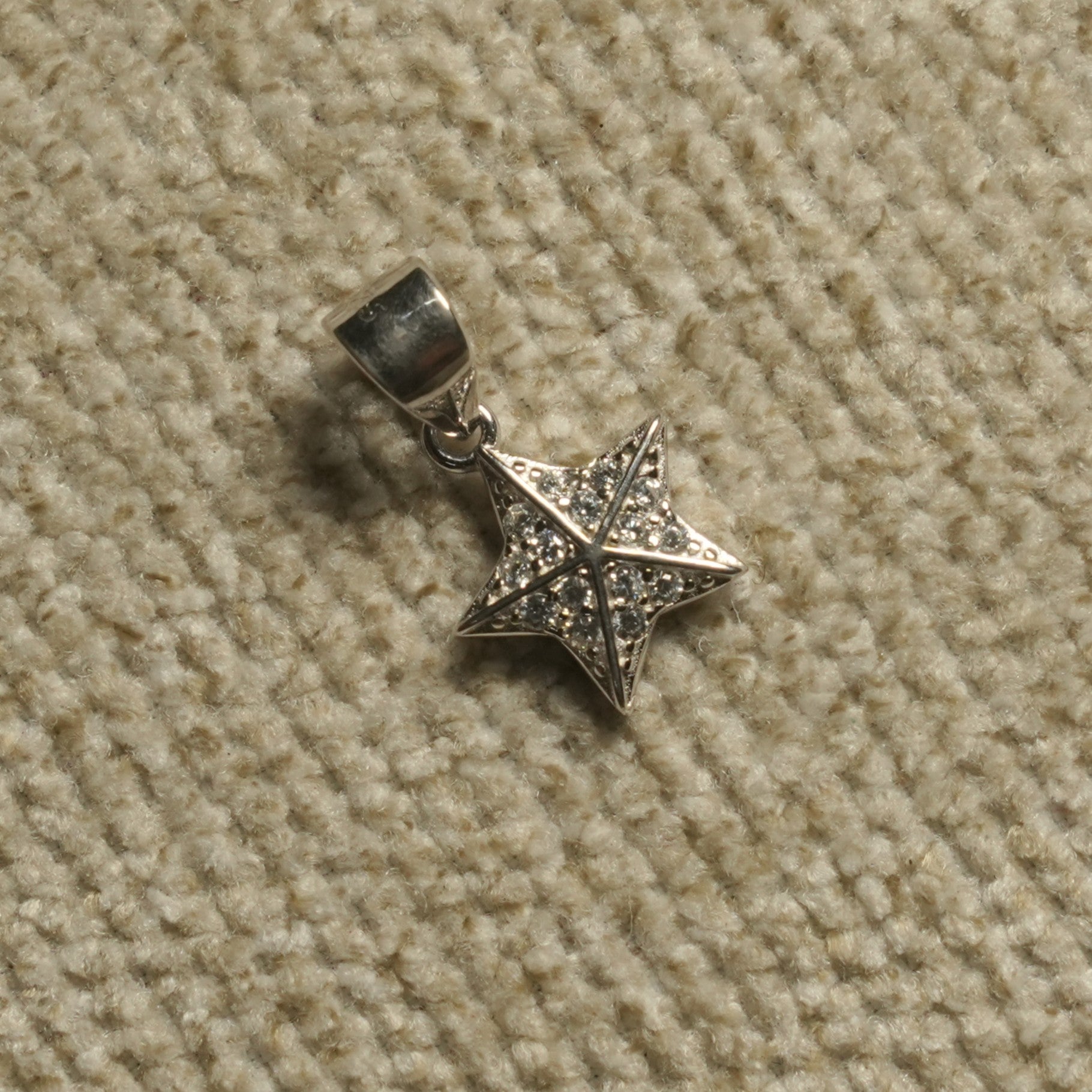 Faceted sterling silver star Pendant set with Bejewelled cubic zirconia, photographed on beige woven fabric.