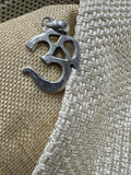 Polished sterling silver Om pendant with openwork curves, resting against woven beige fabric.