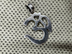Sterling silver Om pendant photographed face up on dotted cream fabric, showing the polished tapered bail.