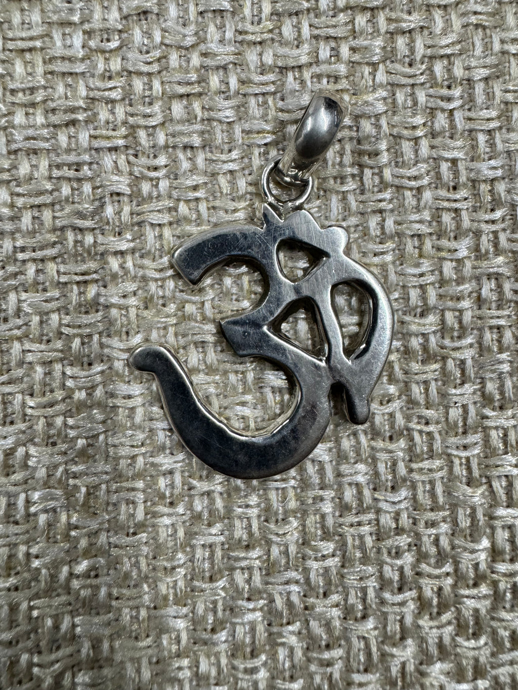 Om pendant in polished sterling silver laid on woven fabric, showing the full outline of the character.