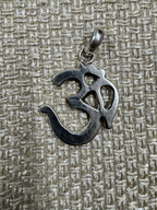 Om pendant in polished sterling silver laid on woven fabric, showing the full outline of the character.
