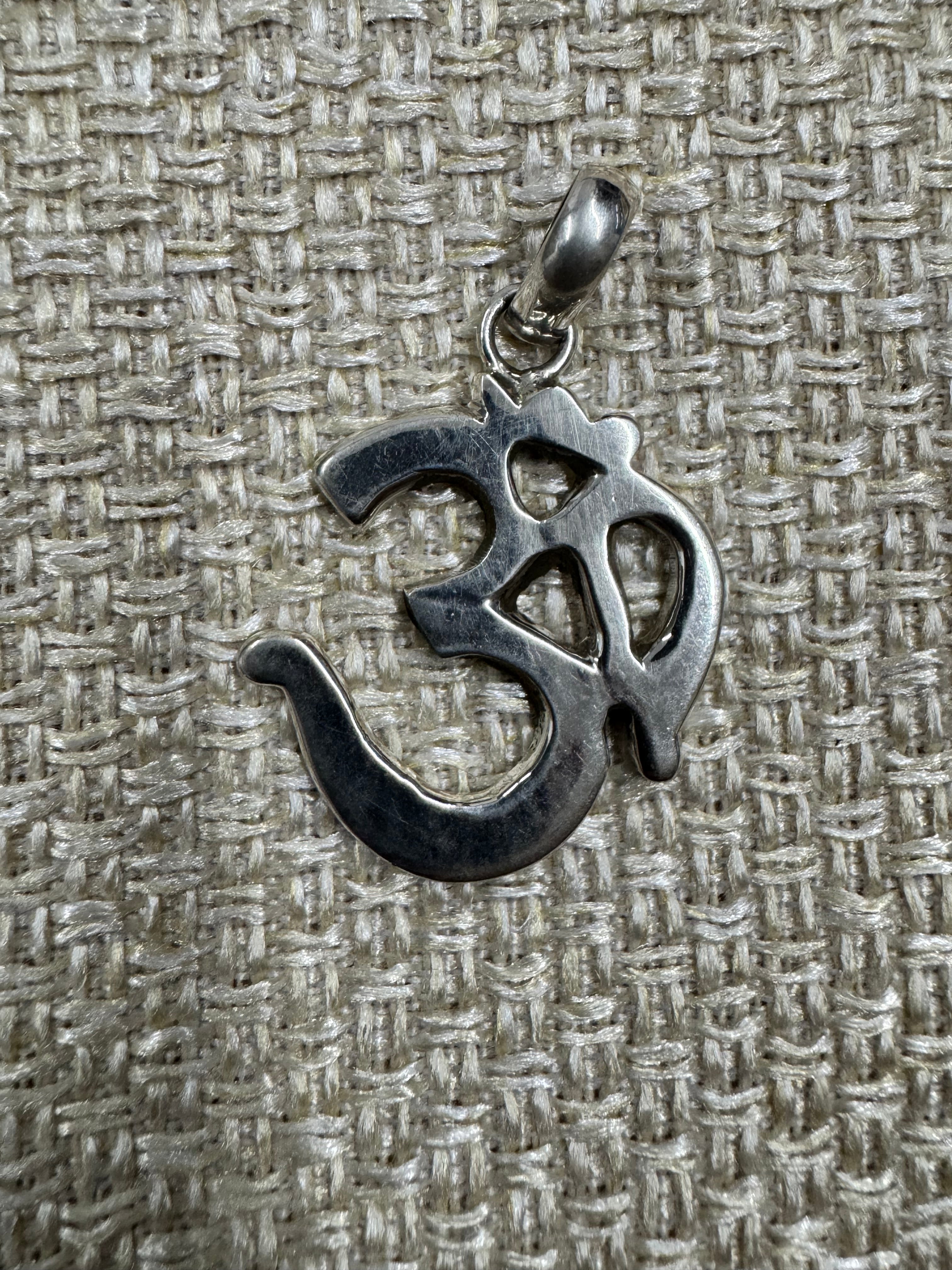 Om pendant in polished sterling silver laid on woven fabric, showing the full outline of the character.