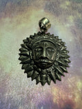Oxidised sterling silver sun disc pendant with pointed rays around a raised face, on a pale iridescent surface.