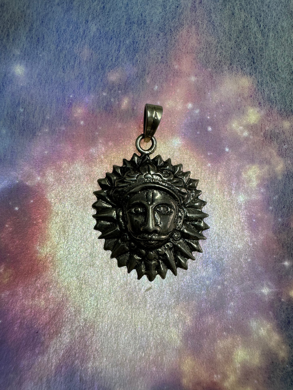 Sterling silver sun disc pendant on a blue and violet iridescent backdrop, the flat bail and jump ring at the rim.