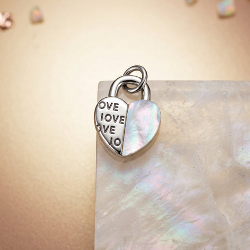 The heart padlock charm standing on a mother of pearl slab.
