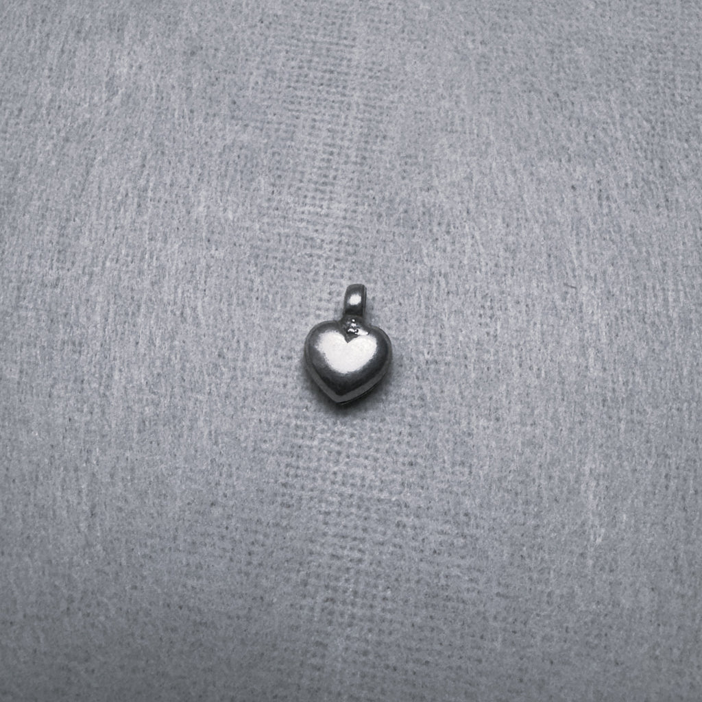 Small sterling silver puffed heart charm pendant with a ring at the top, on a grey surface.