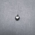 Small sterling silver puffed heart charm pendant with a ring at the top, on a grey surface.