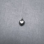 Small sterling silver puffed heart charm pendant with a ring at the top, on a grey surface.