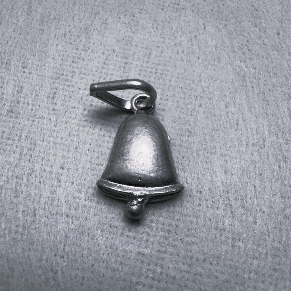 Oxidised sterling silver bell charm pendant with a small clapper and a ring at the top, on a grey surface.