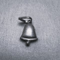 Oxidised sterling silver bell charm pendant with a small clapper and a ring at the top, on a grey surface.