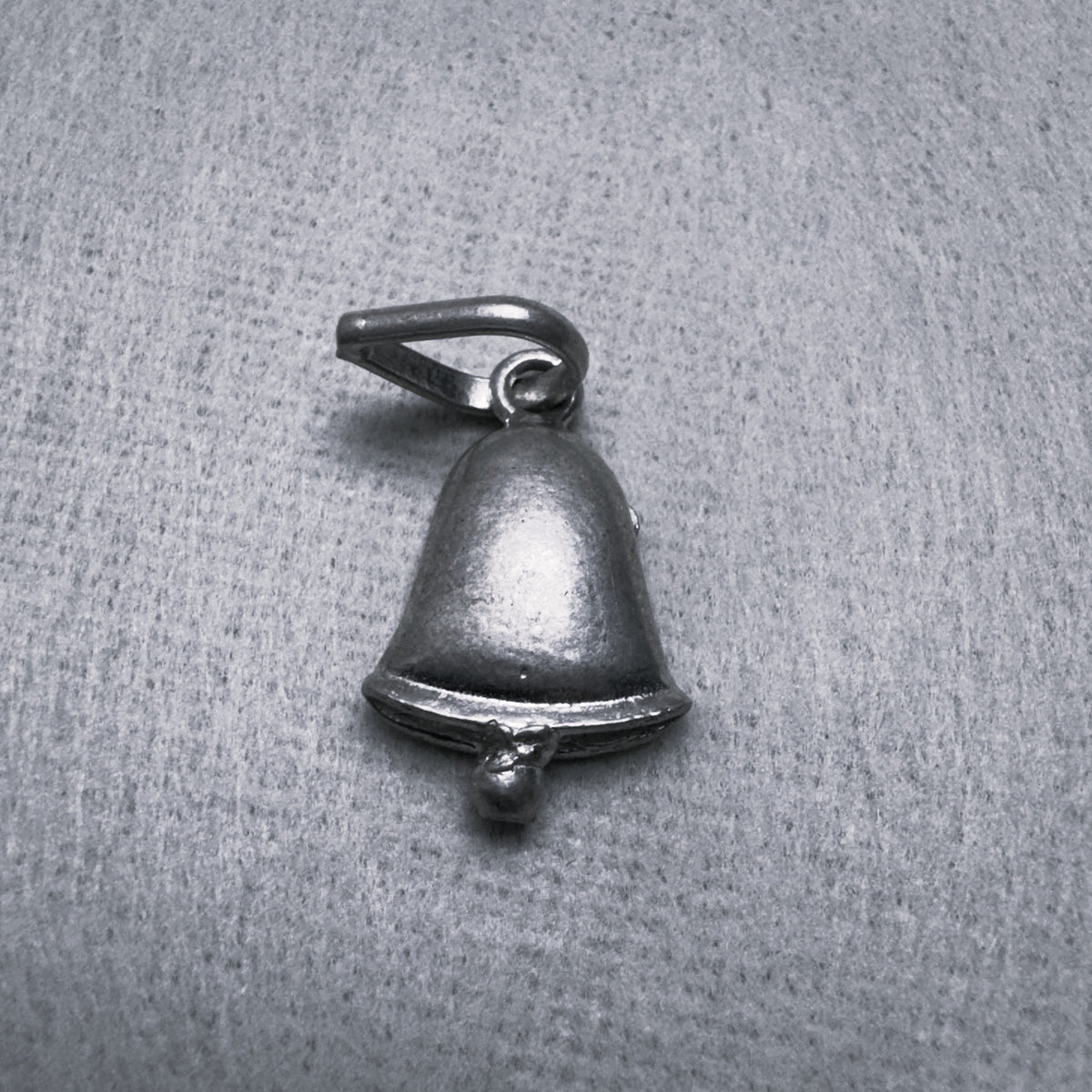 Oxidised sterling silver bell charm pendant with a small clapper and a ring at the top, on a grey surface.