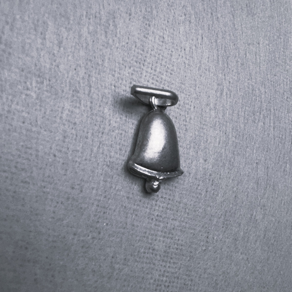 The silver bell charm pendant at a slight angle, showing the curve of the bell.