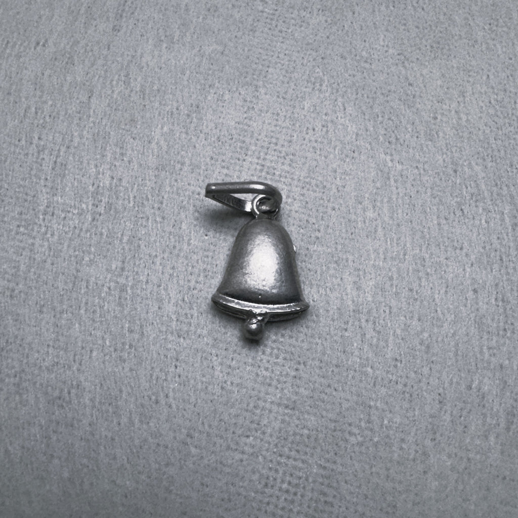 The small oxidised silver bell charm laid flat, bail to the top left.